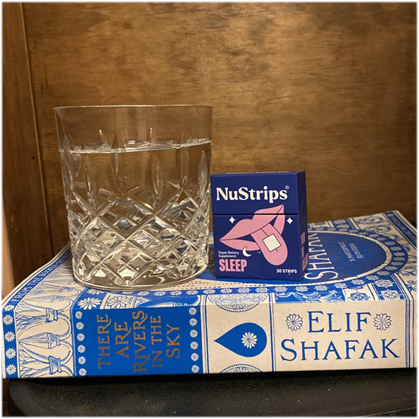 A box of NuStrips sleep strips on a nightstand beside a book &mdash; no water needed
